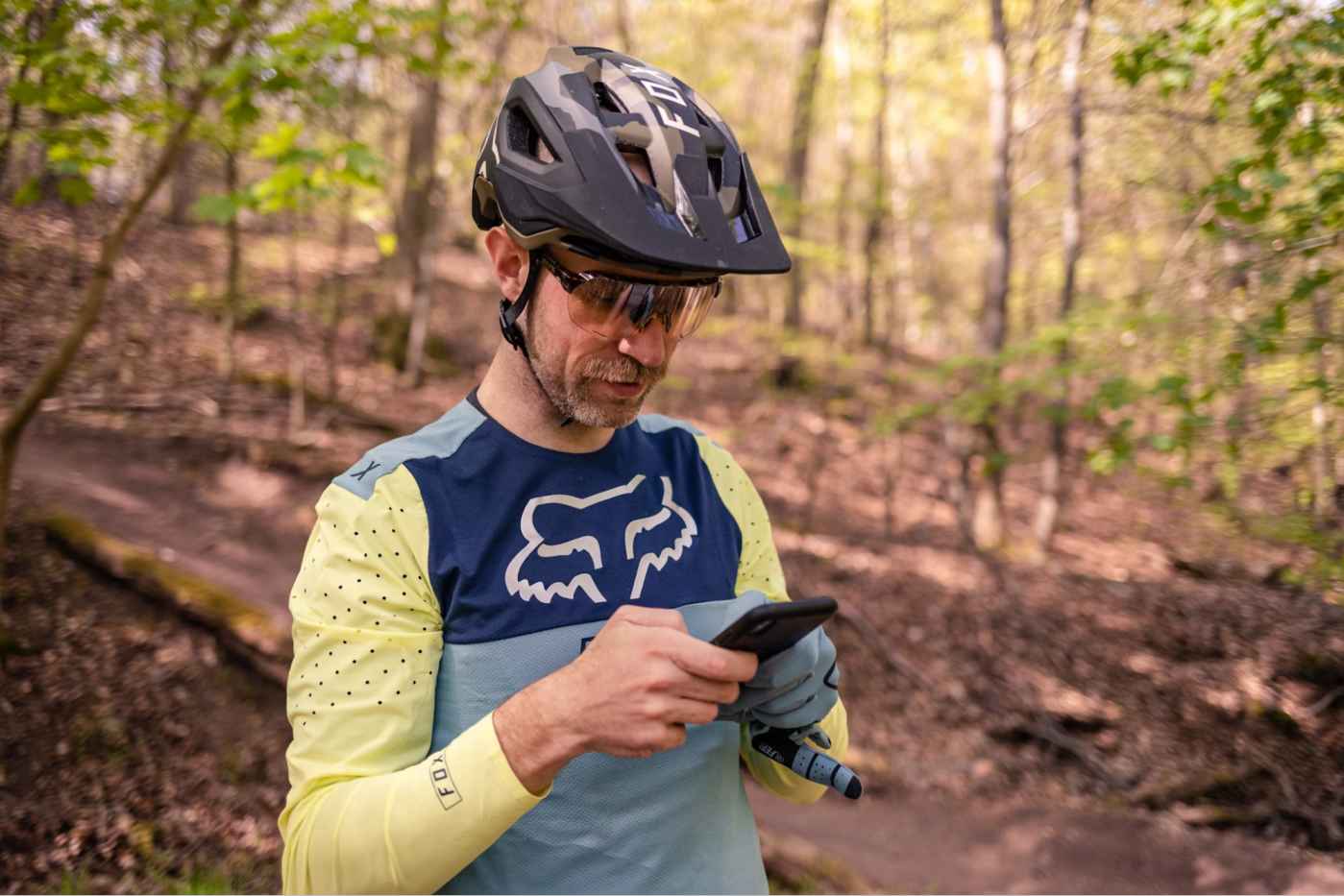 A male mountain biker checking his phone trailside in the forest on a sunny spring day.